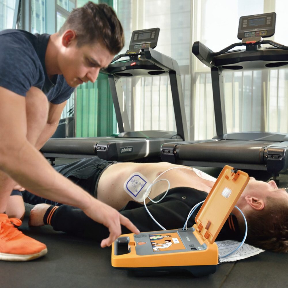 Rescuer operating the Mindray BeneHeart C1A AED with a defibrillation pad applied to a patient's bare chest